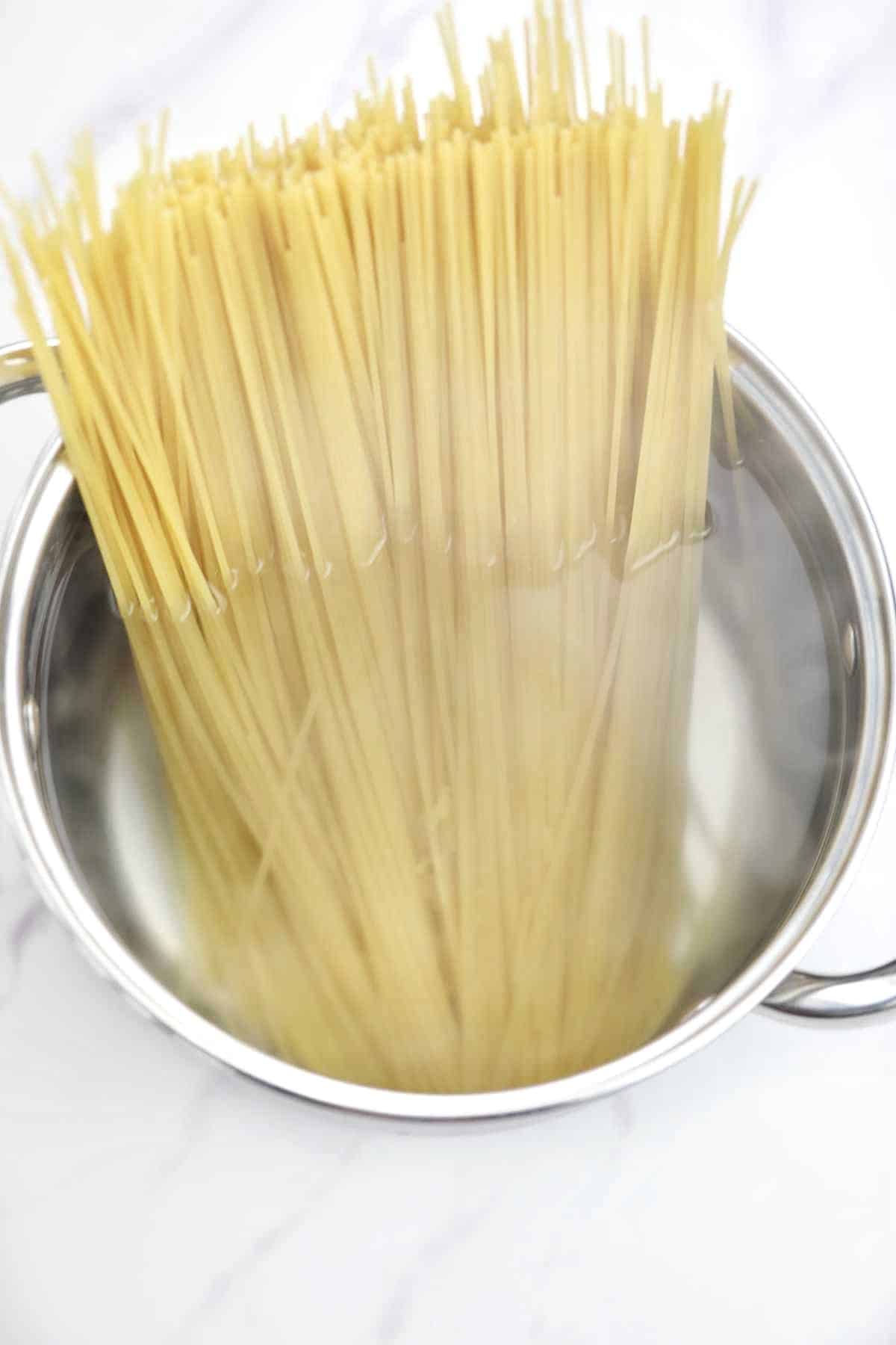spaghetti added to a pot of boiling water.